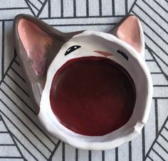 a ceramic cat bowl with red liquid in it's mouth on a patterned surface