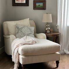 a white chair sitting next to a window in a living room under a painting on the wall