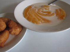 a white plate topped with fried food next to a bowl filled with orange sauce on top of a table