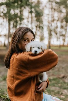 a woman is holding a small white dog in her arms while sitting on the ground