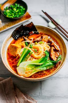 a bowl filled with noodles, meat and vegetables next to chopsticks on a table