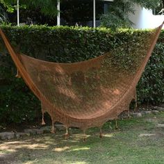 a hammock hanging from a tree in front of a house with bushes behind it