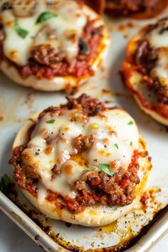 mini pizzas with meat and cheese are on a baking sheet, ready to be eaten