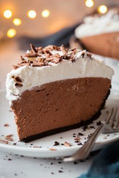 a slice of chocolate pie on a plate with a fork and some lights in the background