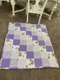 a purple and white quilt sitting on the floor next to two chairs with matching cushions