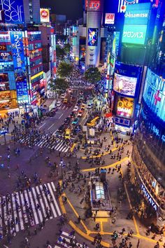 an aerial view of a city at night with many people crossing the street and buildings lit up