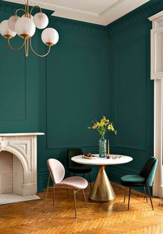 a dining room with green walls and white table surrounded by three chairs, one has a vase filled with flowers on it