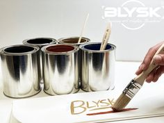 a person holding a paintbrush in front of six cans of paint with the word blysk on it