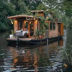 a house boat floating on top of a lake surrounded by trees and greenery in the water