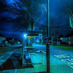 a bus stop sitting on the side of a road next to a street light at night