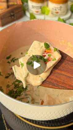 a wooden spoon in a pot filled with soup and garnished with parsley