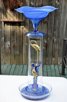 a blue glass vase sitting on top of a white table next to a wooden fence