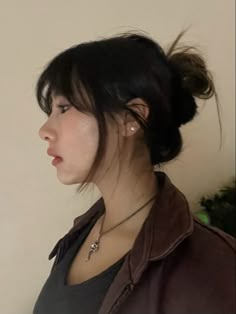 a woman with black hair wearing a brown leather jacket and silver necklace looking off into the distance