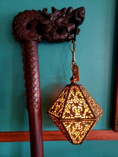 a lamp hanging from the side of a blue wall next to a wooden pole with an ornate design on it