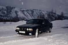 a black car parked in the middle of snow covered ground with mountains in the background