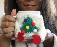 a woman holding up a knitted christmas tree mug cozy