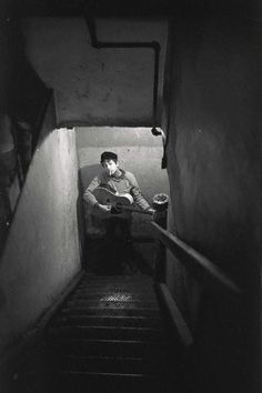 black and white photograph of man playing guitar down stairs