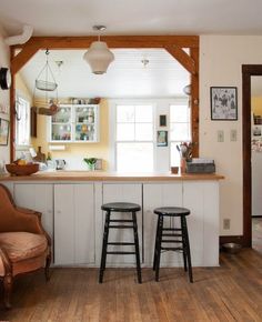 two stools sit in front of the bar area at this kitchen counter with white cabinets and wood floors