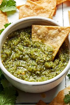 guacamole and tortilla chips in a white bowl with cilantro on the side