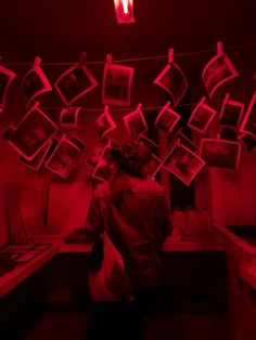 a person standing in a room with pictures hanging from the ceiling and red light shining on them