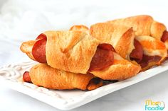 two hotdogs on croissants sitting on a white plate