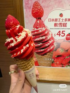 a person holding an ice cream cone with strawberries on it in front of a poster