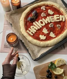 a homemade pizza with the word halloween spelled on it, surrounded by candles and lemon slices