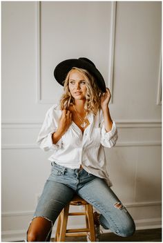 a woman sitting on top of a wooden stool wearing a cowboy hat and denim shorts