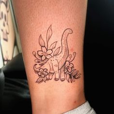 a small dinosaur with flowers on its back leg tattoo design for women's legs