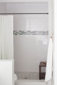 a white tiled bathroom with a bench and shower