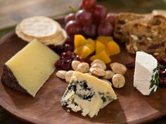 a wooden plate topped with different types of cheese and crackers next to grapes, nuts