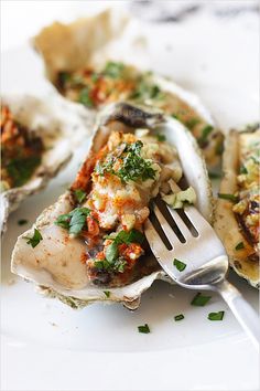 an open oyster shell on a white plate with a fork in it and other food items