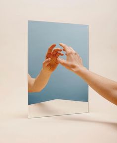 two hands reaching out to each other in front of a mirror with the reflection of someone's hand on it