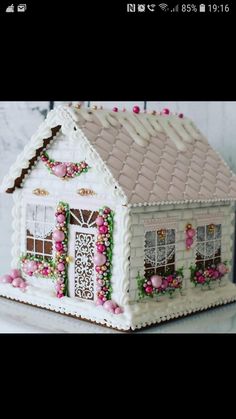 a small white house with pink flowers on the roof and windows is decorated in frosting