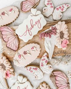 cookies decorated with pink and white butterflies are arranged on a wooden board that says, always