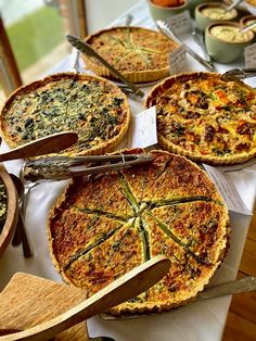 several different types of pies on display at a buffet table with wooden utensils