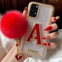 a woman's hand holding a phone case with a red pom - pom