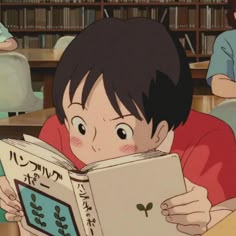 a young boy reading a book while sitting at a table in front of other children