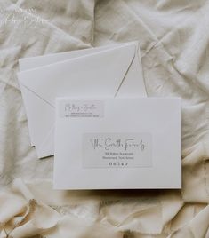 two envelopes sitting on top of a bed covered in white sheets and paper with writing