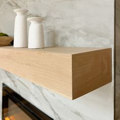 two white vases sitting on top of a wooden shelf next to a fire place