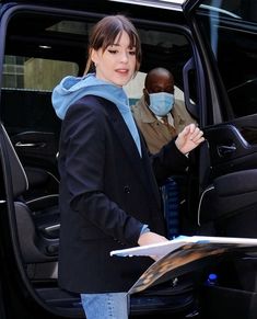 a woman wearing a face mask standing in the back of a vehicle while holding a clipboard