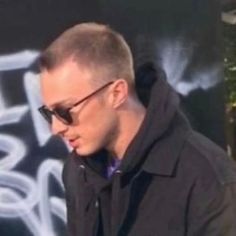 a man in sunglasses is looking down at his cell phone while standing next to a graffiti covered wall