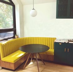 a yellow bench sitting in front of a window next to a table and cupboards