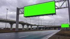 an empty highway with green screen billboards on the side and cars driving down it