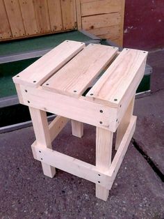 a small wooden stool sitting on top of a cement floor next to a green door