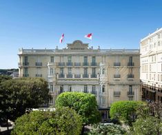 an old building with flags on top and trees in the foreground