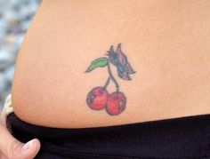 a woman's stomach with a tattoo of cherries on the back of her belly