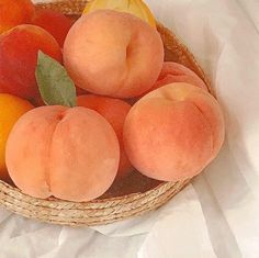 a basket filled with peaches and oranges on top of a white table cloth