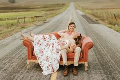 two women sitting on an orange couch in the middle of a road with a blanket draped over them