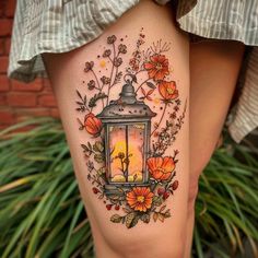 a woman's thigh with flowers and a lantern tattoo on her leg, which is lit up